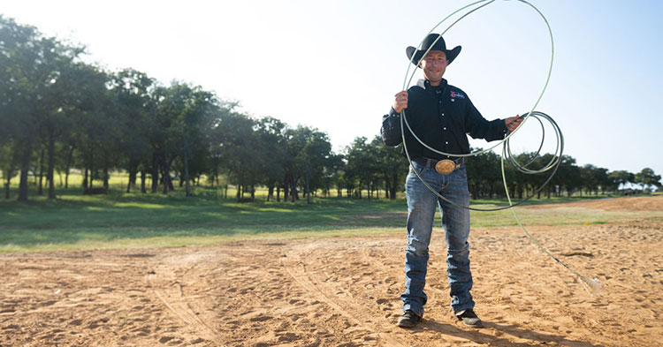 Haven Meged standing in an arena, holding a rope wearing a black shirt and black cowboy hat.